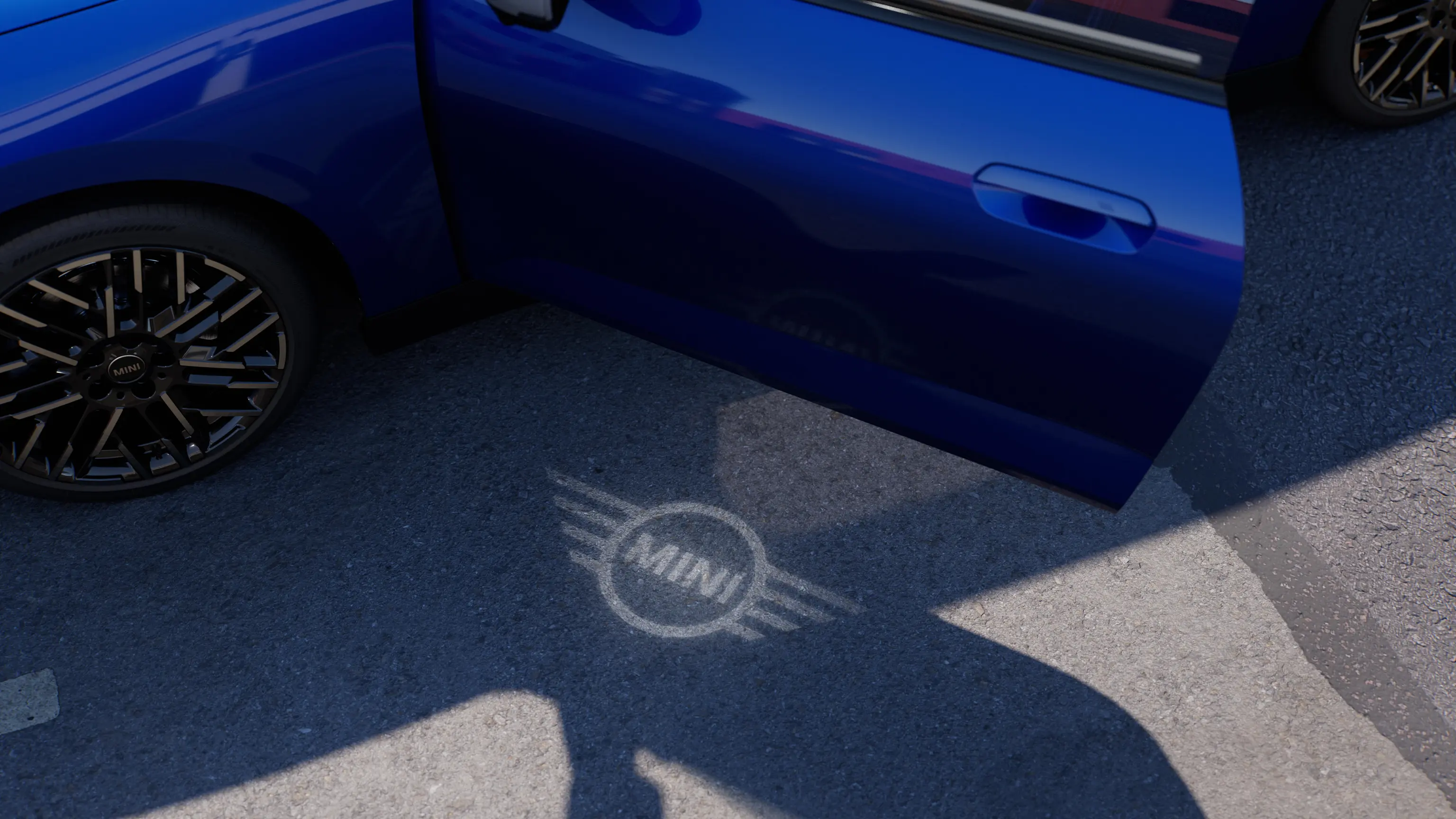 Ulkokuva täyssähköisestä MINI Cooperista, jonka ovi on auki ja jonka MINI-logoa esittävä tervehdysvalo näkyy maassa