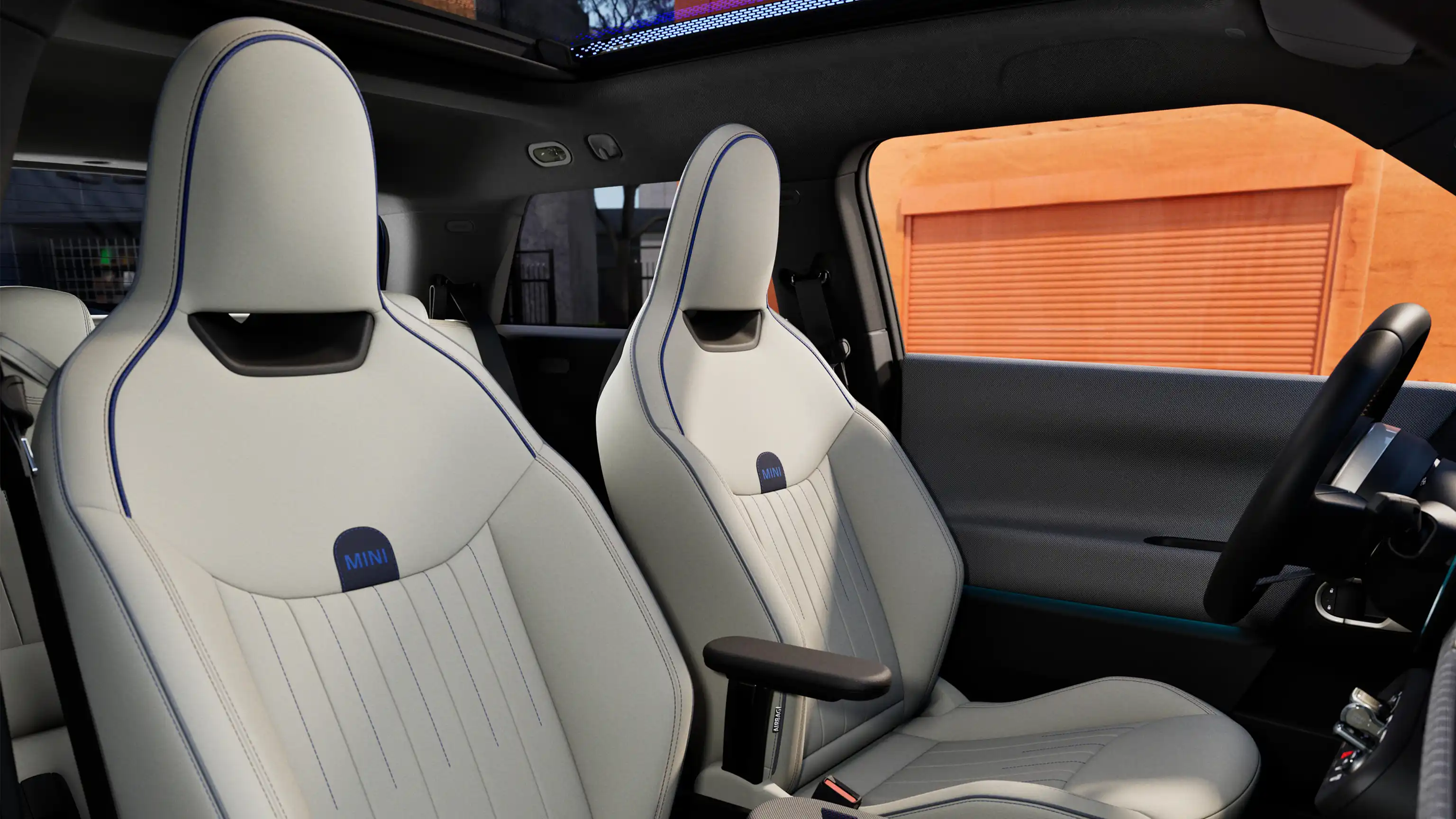Täyssähköisen MINI Cooperin sisäkuva, jossa näkyy kojelauta, ohjauspyörä, pyöreä näyttö, lasikatto ja etuistumien takaosat