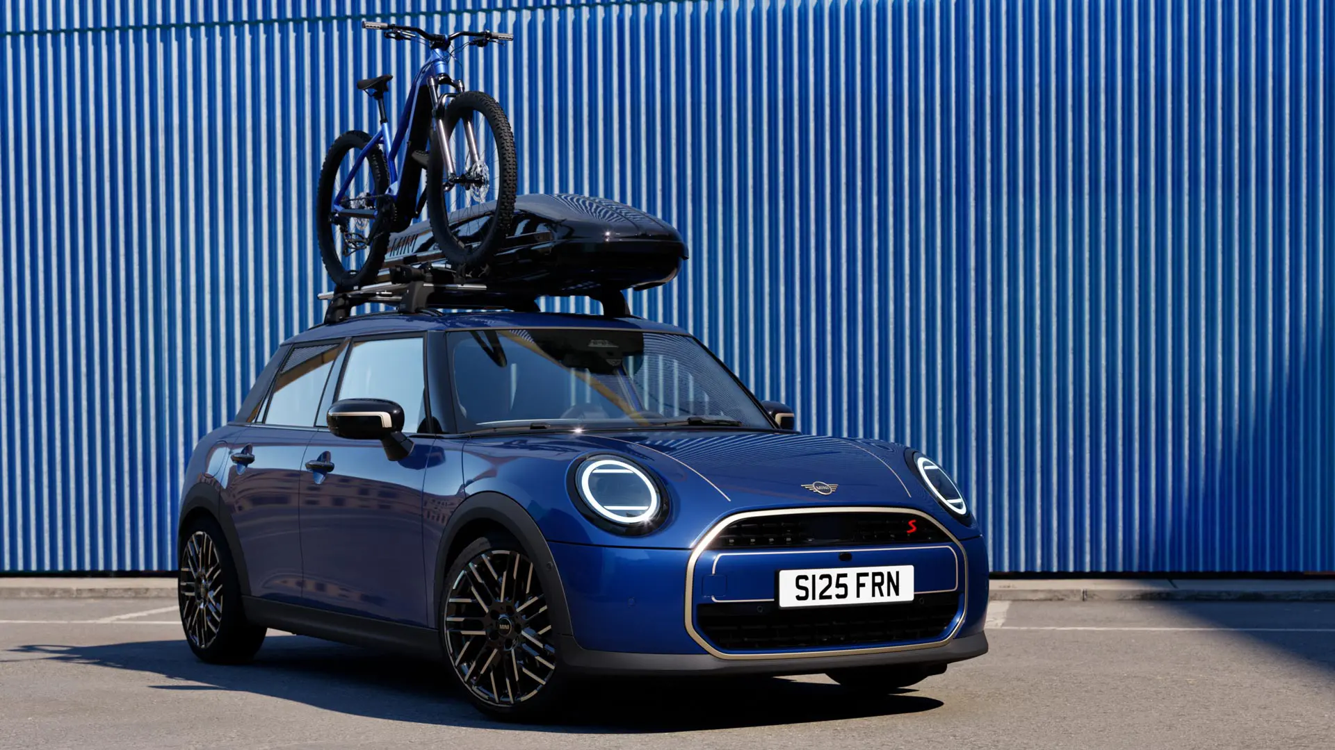 Kuva edestä Indigo Sunset Blue -värisestä MINI Acemanista MINI-kattopyörätelineellä, jossa on maastopyörä ja MINI-kattoboksi 320.