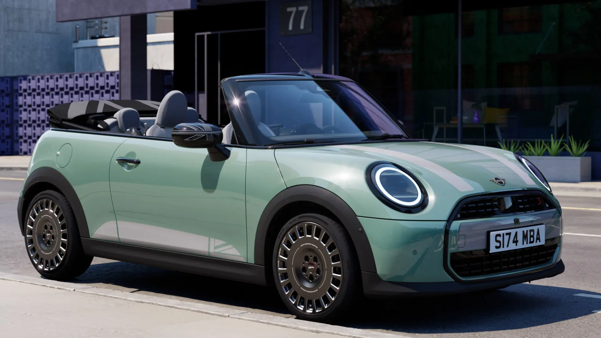 Kuva edestä sivulta Ocean Wave Green -värisestä MINI-avoautosta valkoisilla MINI Heritage -konepeltitarroilla. 