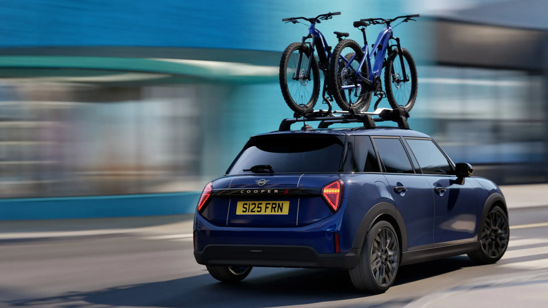 MINI Aceman Indigo Sunset Blue -värissä, varustettuna MINI-kattopyörätelineellä, jossa on kaksi maastopyörää, kolme neljäsosan takanäkymä. 