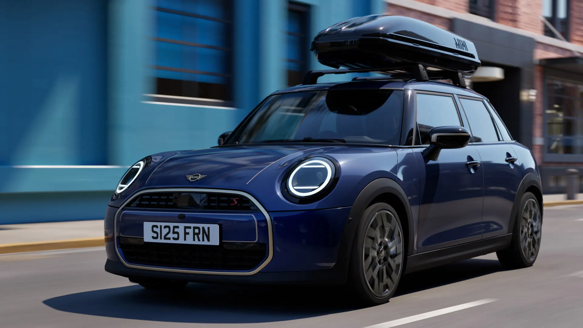 Kolmen neljänneksen kuva edestä Indigo Sunset Blue -värisestä MINI Acemanista MINI-kattotelineellä, jossa on MINI-kattoboksi 320. 
