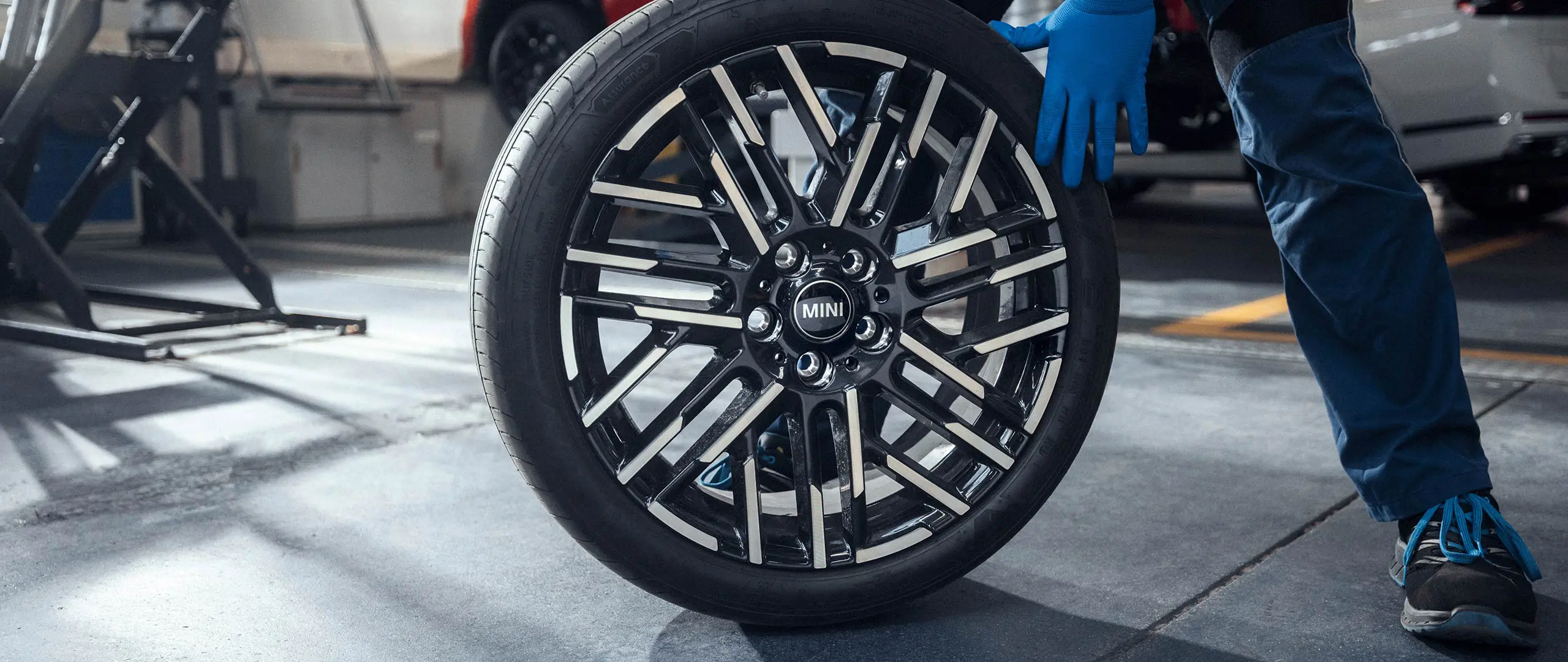 MINI Partnerin huoltomekaanikko pyörittää 18" Night Flash Spoke Bicolour ‑kevytmetallivanteen paikalleen.