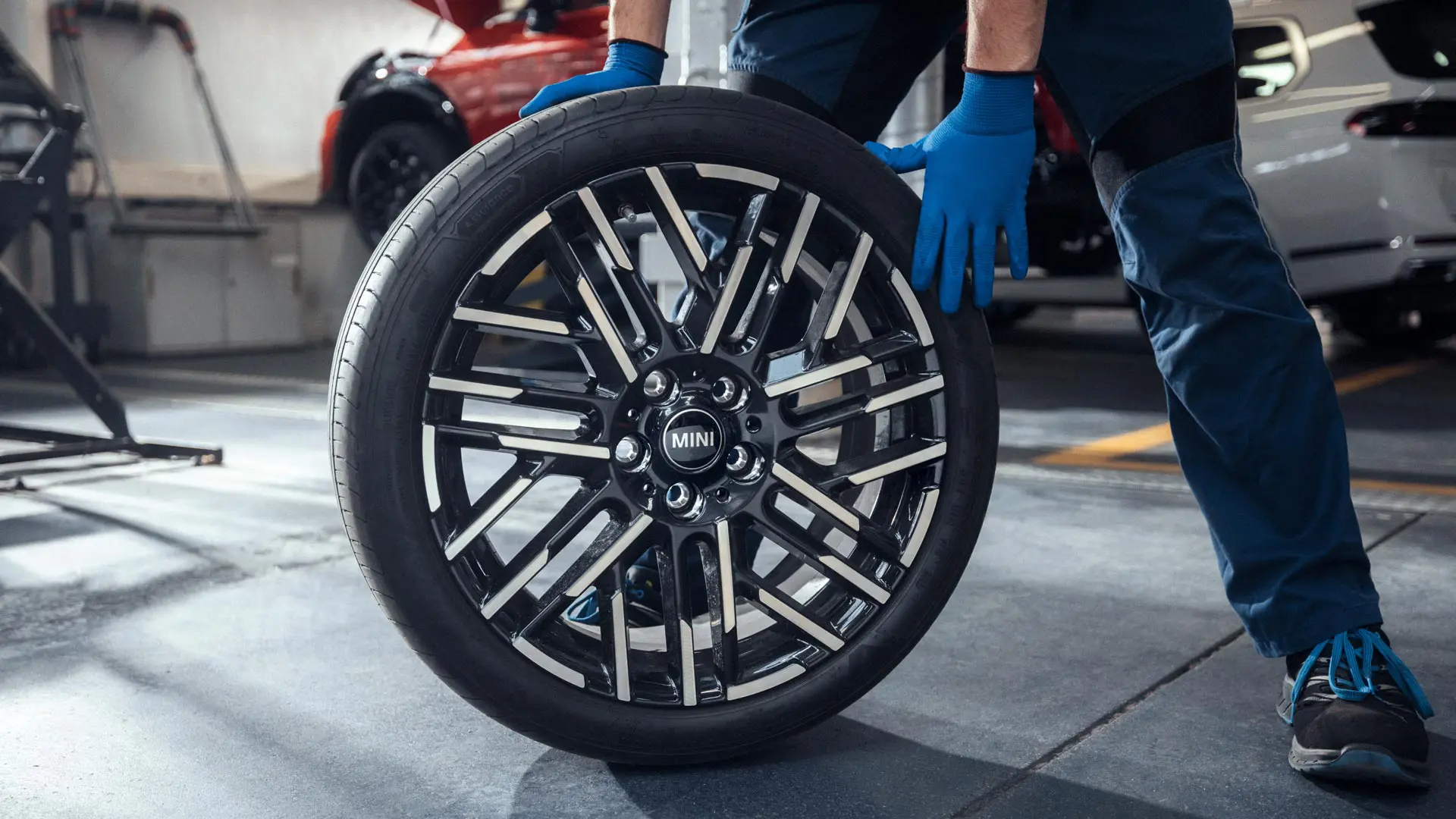 MINI Partnerin huoltomekaanikko pyörittää 18" Night Flash Spoke Bicolour ‑kevytmetallivanteen paikalleen.