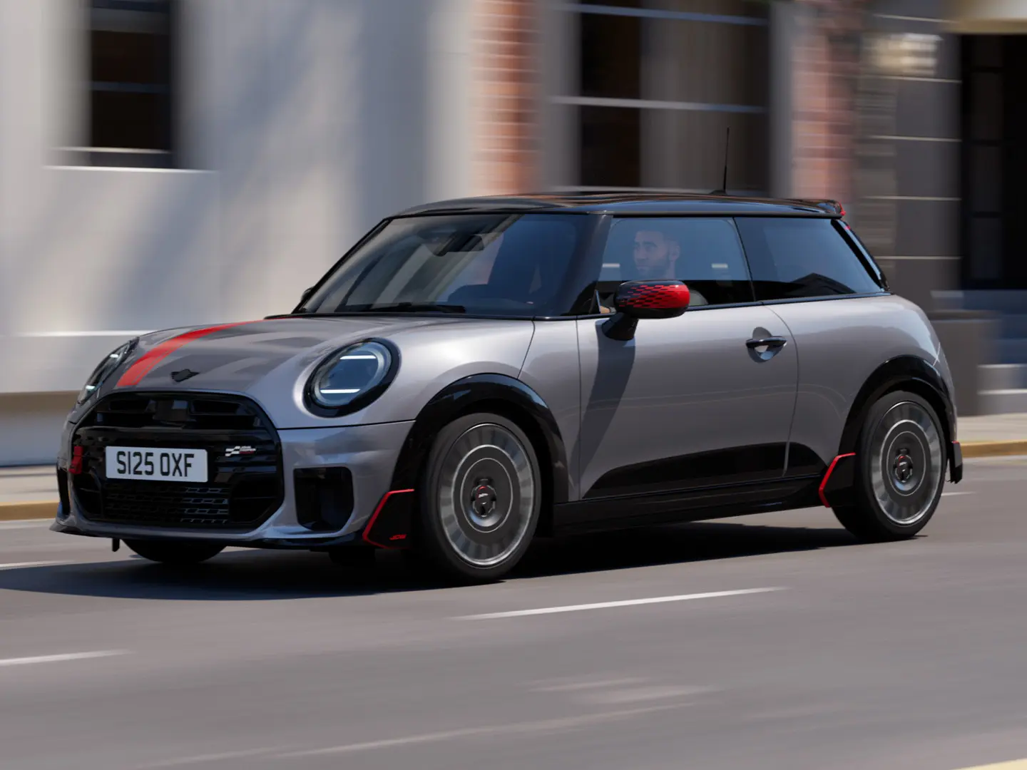 MINI Cooper, 3-ovinen, väri Melting Silver, Chili Red ‑väriset John Cooper Works ‑peilinkuoret ja konepeltitarra, musta kattospoileri ja siiveke, ajaa kaupungilla katua pitkin – näkymä edestä.