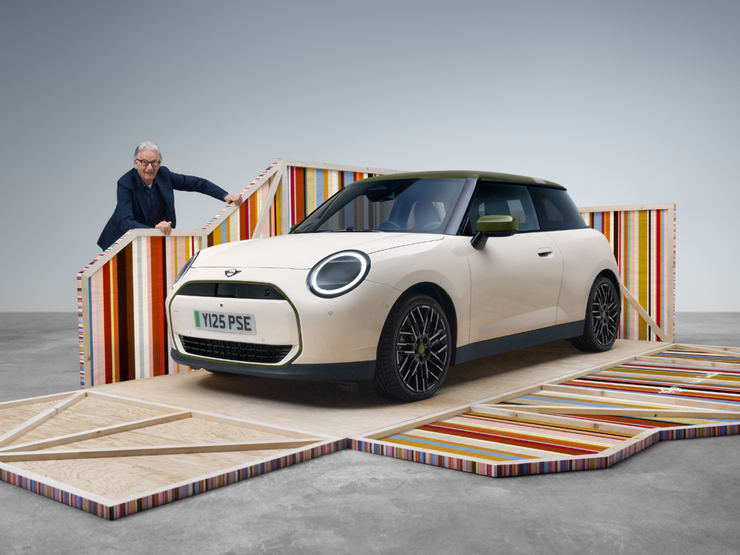 Sivukuva edestä täyssähköisestä MINI Cooper Paul Smith Editionista Inspired White -sävyssä, vierellä suunnittelija Paul Smith