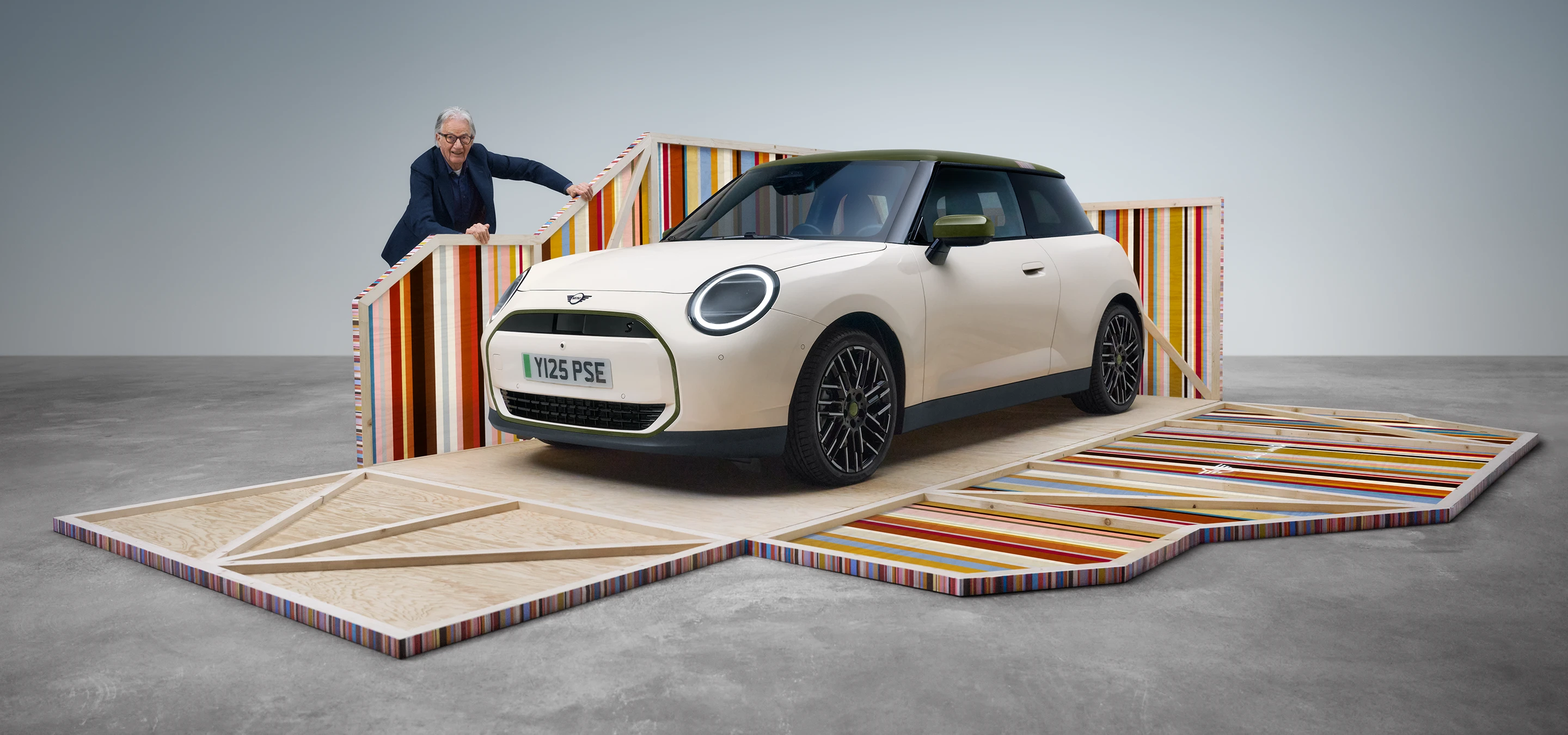 Sivukuva edestä täyssähköisestä MINI Cooper Paul Smith Editionista Inspired White -sävyssä, vierellä suunnittelija Paul Smith